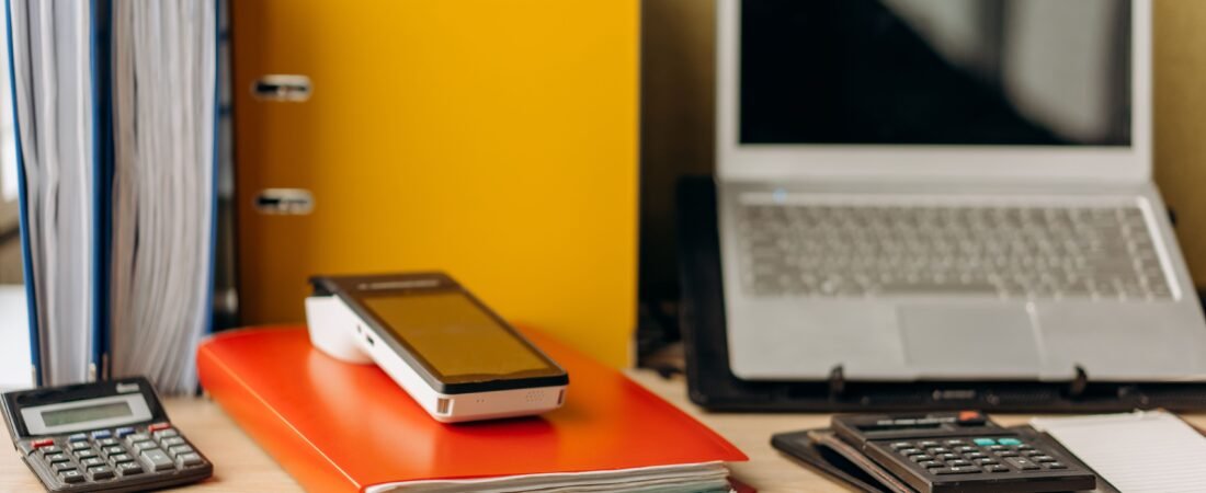 Office desk setup with laptop, documents, and calculators, ideal for business productivity.
